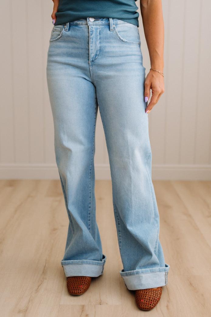 Woman wearing a striped tank top and light blue jeans standing against a neutral wall.