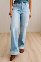 Woman wearing a striped tank top and light blue jeans standing against a neutral wall.