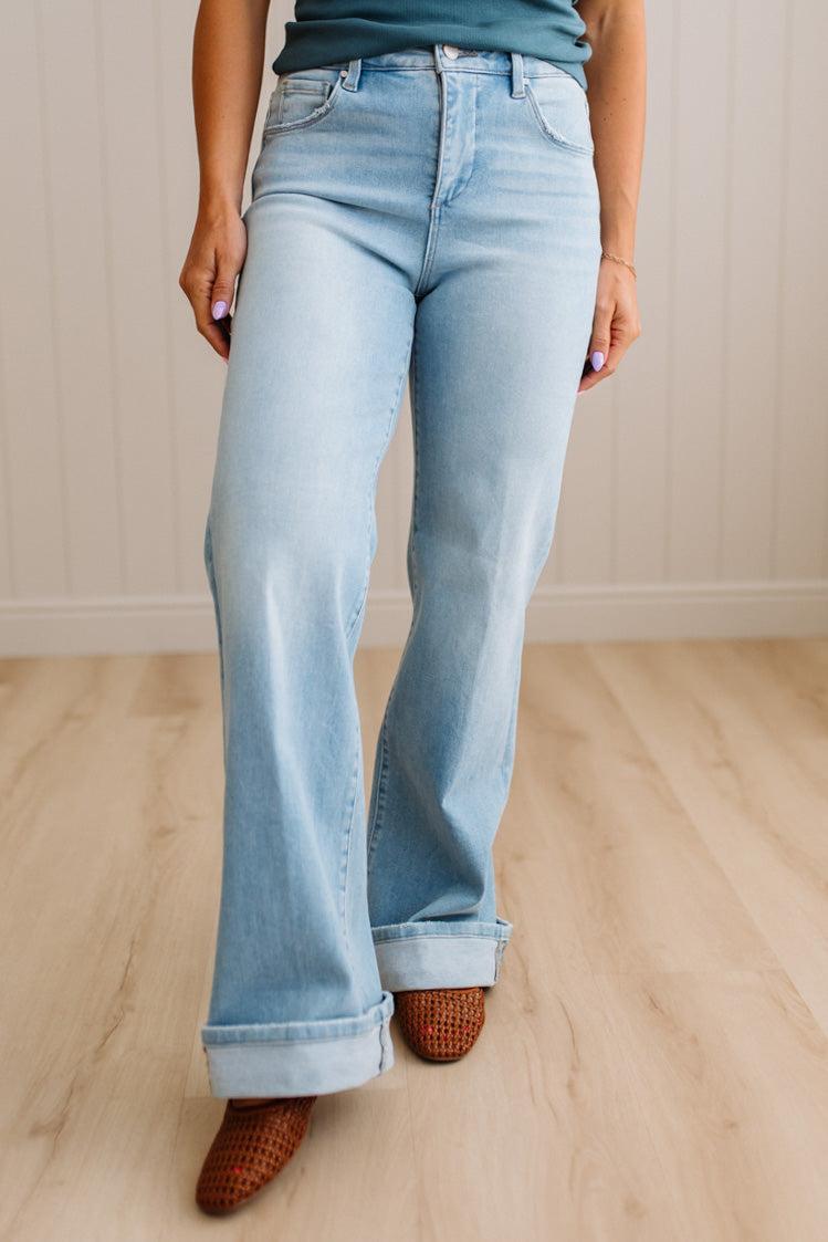 Woman wearing a striped tank top and light blue jeans standing against a neutral wall.