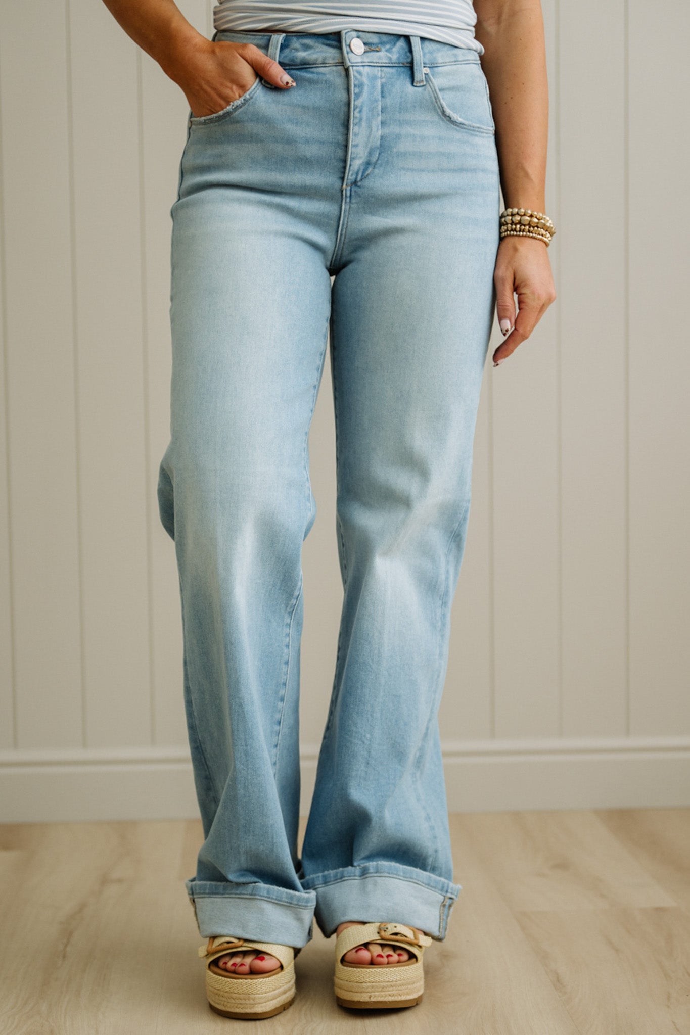 Light blue jeans worn by a person on a wooden floor with a white paneled wall background