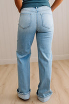 Woman wearing a striped tank top and light blue jeans standing against a neutral wall.