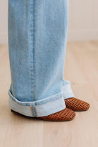 Woman wearing a striped tank top and light blue jeans standing against a neutral wall.