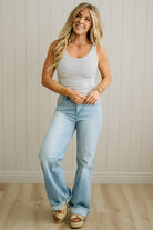 Woman wearing a striped tank top and light blue jeans standing against a neutral wall.
