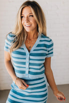 Blonde woman wearing a light blue and medium blue horizontal striped top with button front sweater and short sleeves.