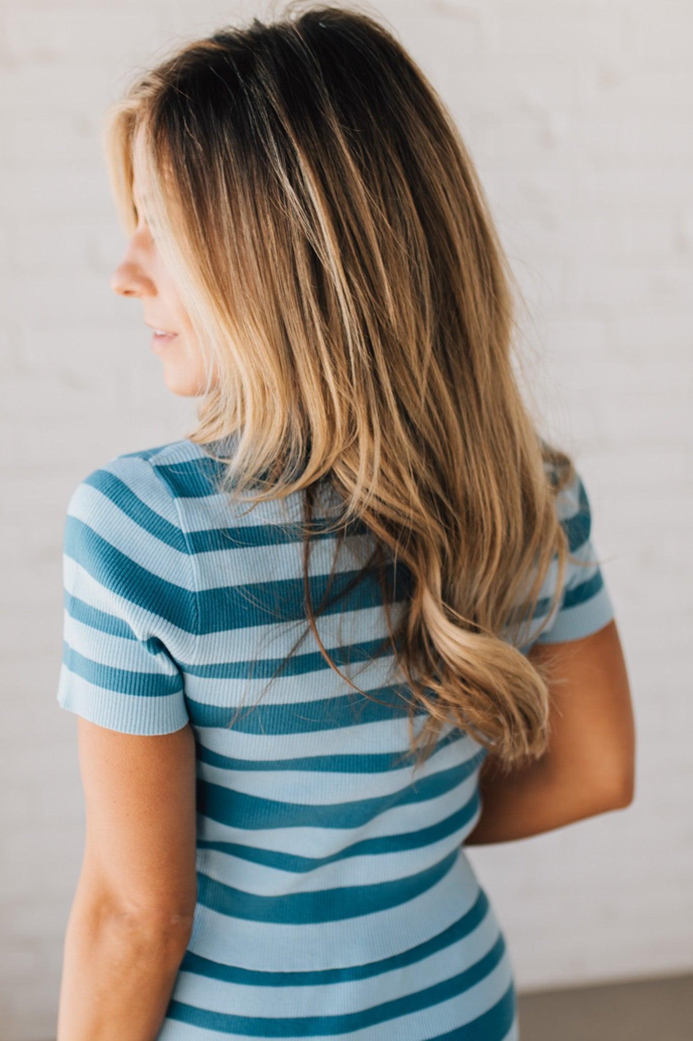 Blonde woman wearing a light blue and medium blue horizontal striped top with button front sweater and short sleeves.