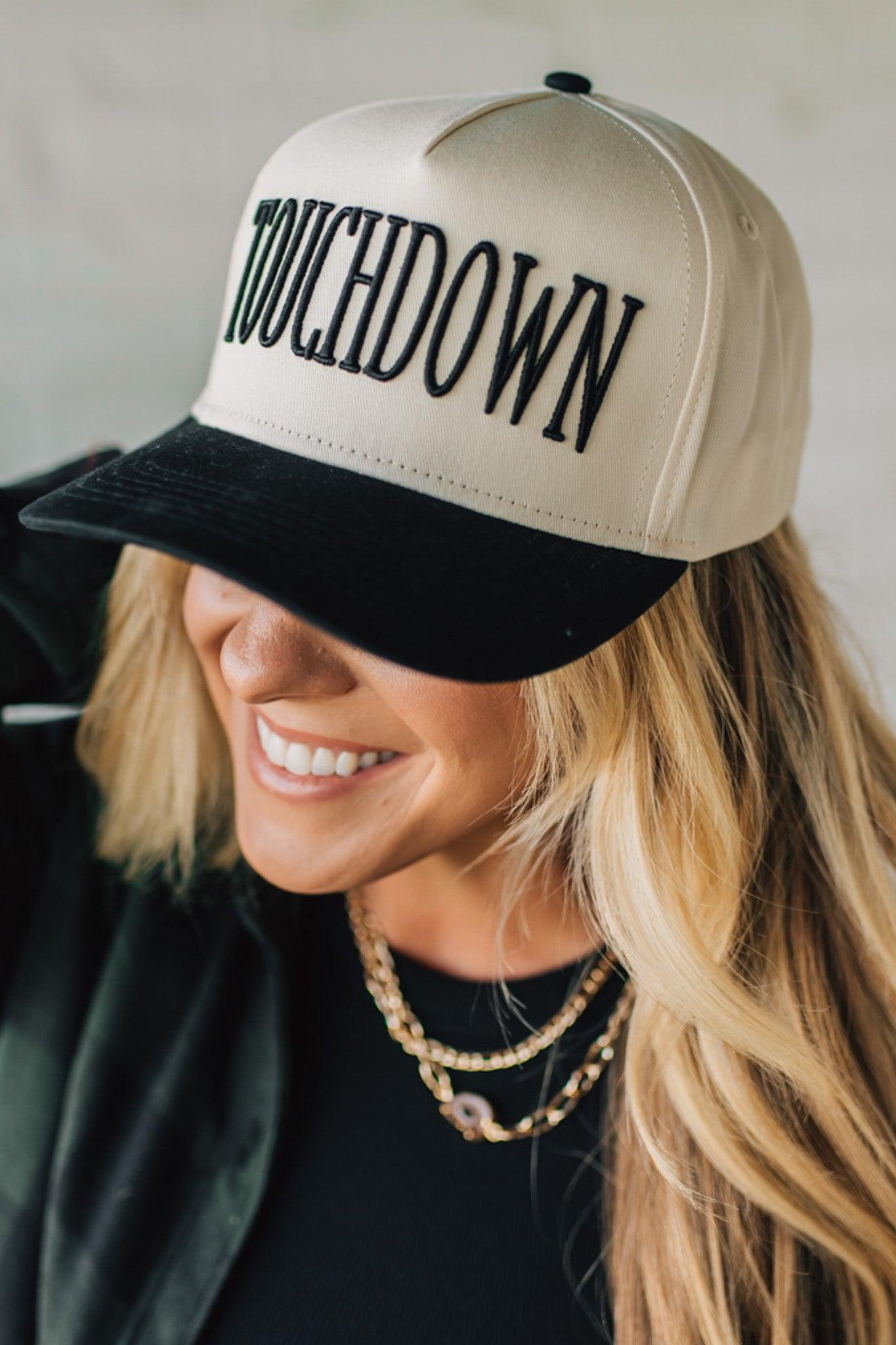 Woman wearing a beige and black cap with 'TOUCHDOWN' text on a neutral background