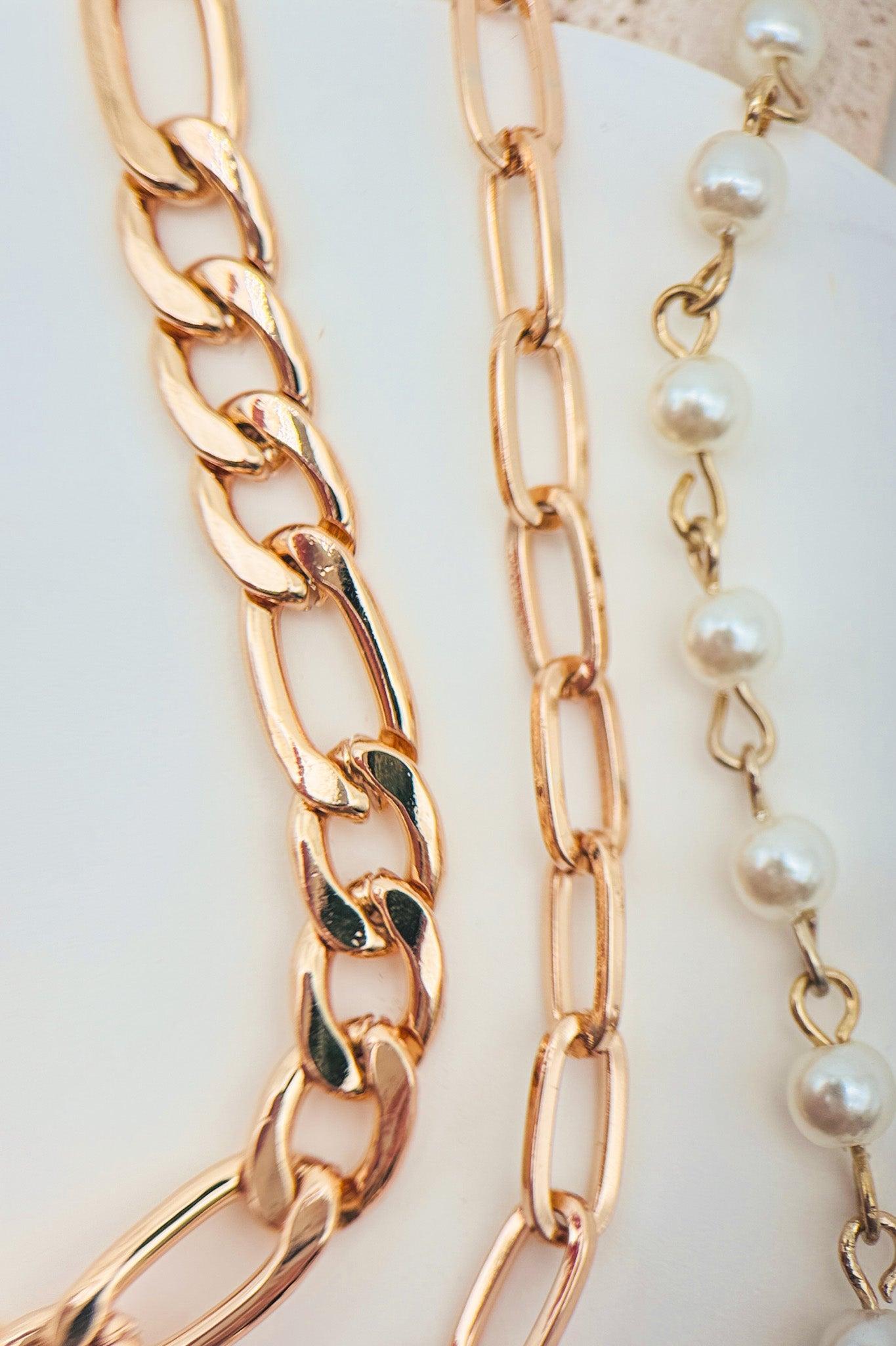 Two gold chain necklaces with a pearl necklace on a white surface