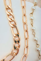 Two gold chain necklaces with a pearl necklace on a white surface