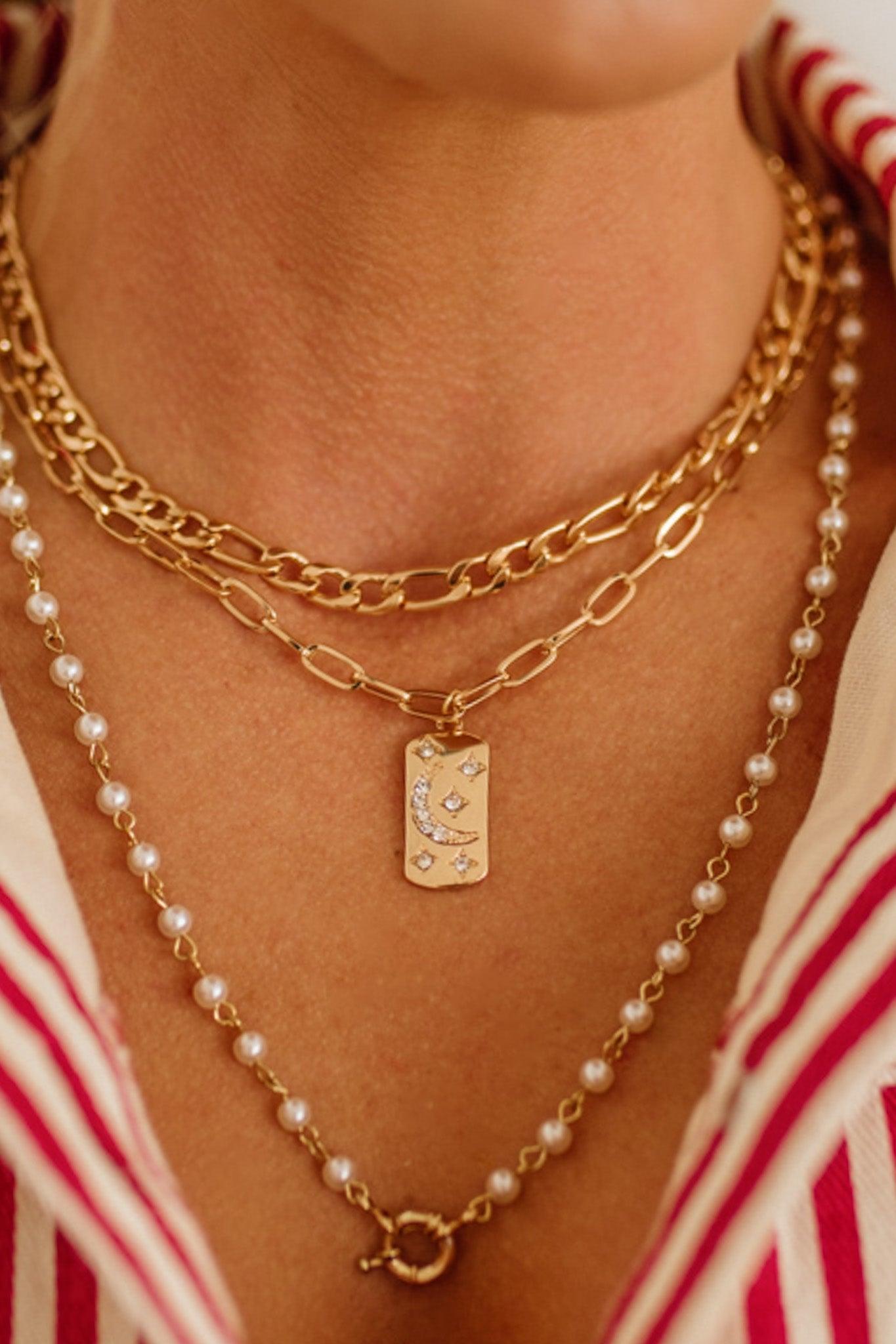 Gold chain necklace with a pendant and pearl necklace on a person wearing a red and white striped garment.