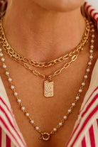 Gold chain necklace with a pendant and pearl necklace on a person wearing a red and white striped garment.