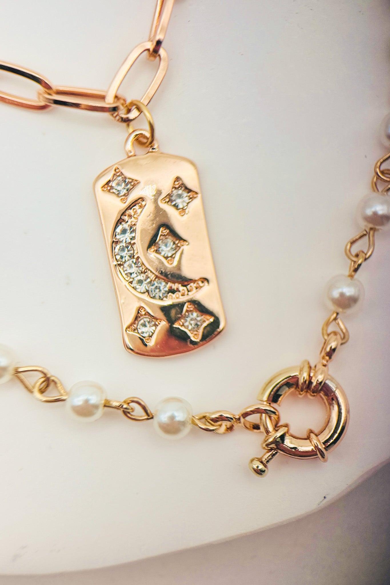 Gold bracelet with a decorative tag and pearl beads on a white background