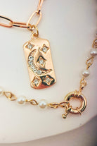 Gold bracelet with a decorative tag and pearl beads on a white background