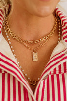 Close-up of a person wearing multiple gold necklaces with a red and white striped shirt.