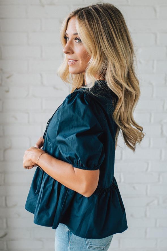Woman wearing a teal blouse against a white brick wall