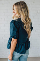 Woman wearing a teal blouse with puffed sleeves against a white brick wall.