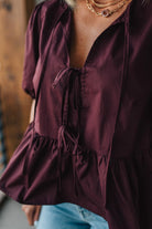 Close-up of a burgundy blouse with ruffled details and a blurred background