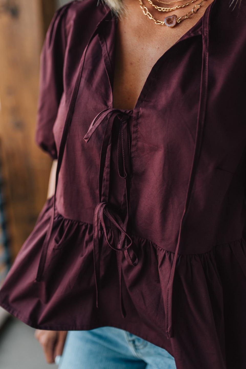Close-up of a burgundy blouse with ruffled details and a blurred background
