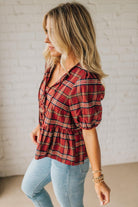 Woman wearing a red plaid shirt and light blue jeans against a white brick wall.