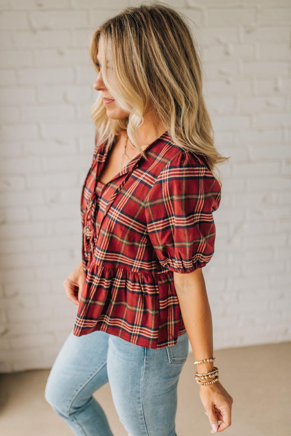 Woman wearing a red plaid shirt and light blue jeans against a white brick wall.