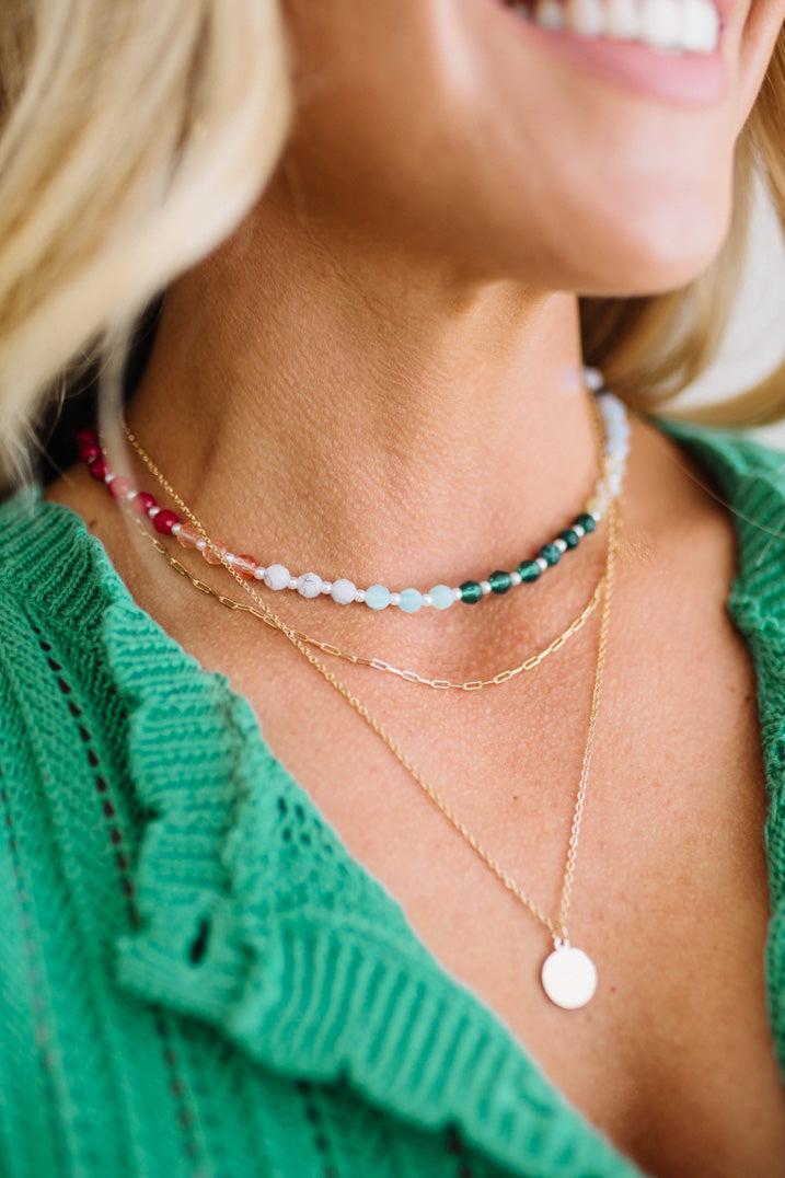 Close-up of a person wearing multiple necklaces with a green top.