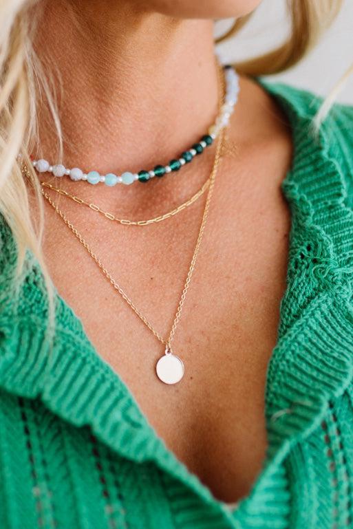 Close-up of a person wearing layered necklaces with a green sweater.