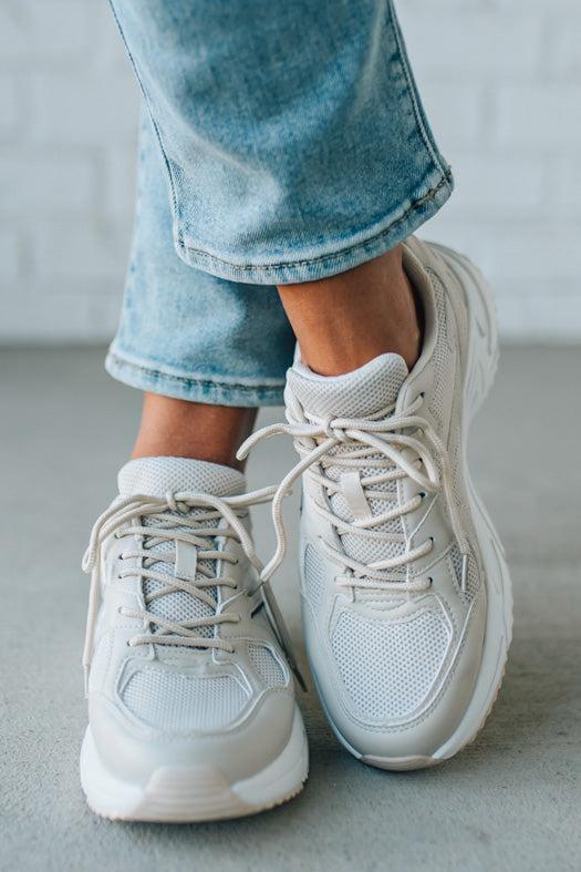 White sneakers worn with light blue jeans on a neutral background