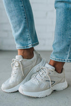 White sneakers worn with light blue jeans on a neutral background