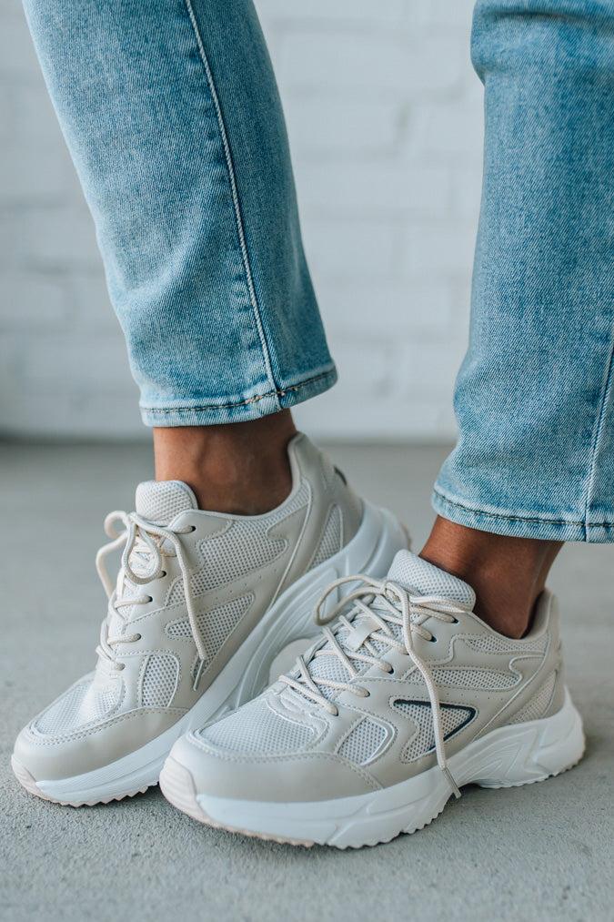 White sneakers worn with light blue jeans on a neutral background