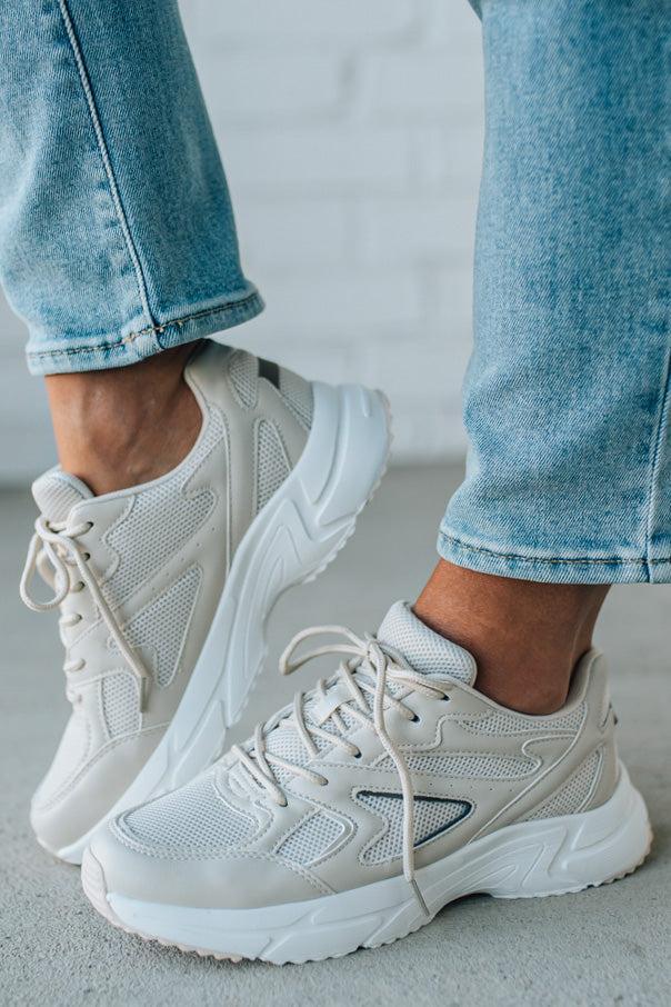 White sneakers worn with light blue jeans on a neutral background
