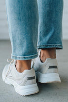 White sneakers with black accents worn with blue jeans on a neutral background
