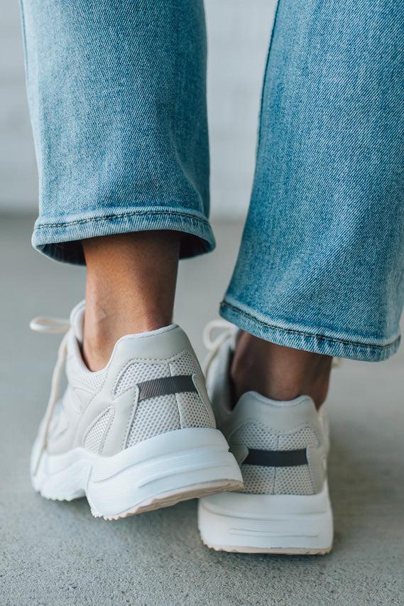White sneakers with black accents worn with blue jeans on a neutral background
