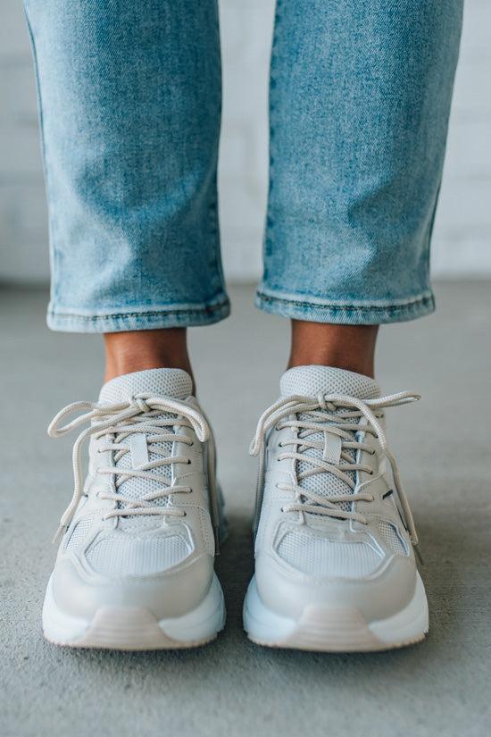 White sneakers worn with light blue jeans on a neutral background