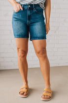 WOMAN WEARING DARK WASH MID-THIGH DENIM SHORT PANTS AND SANDALS.