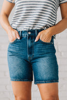 WOMAN WEARING DARK WASH MID-THIGH DENIM SHORT PANTS AND SANDALS.