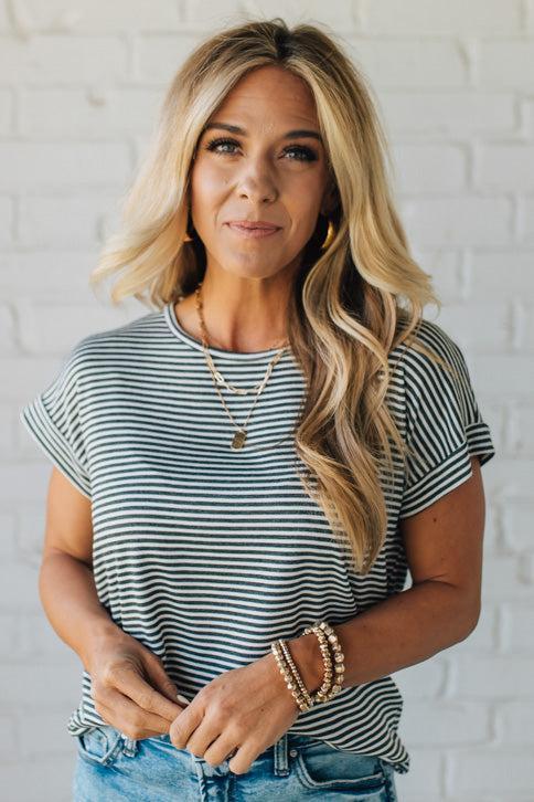 Blonde woman wearing a charcoal grey and white horizontal striped tee with a twist back keyhole accent across the back shoulders.