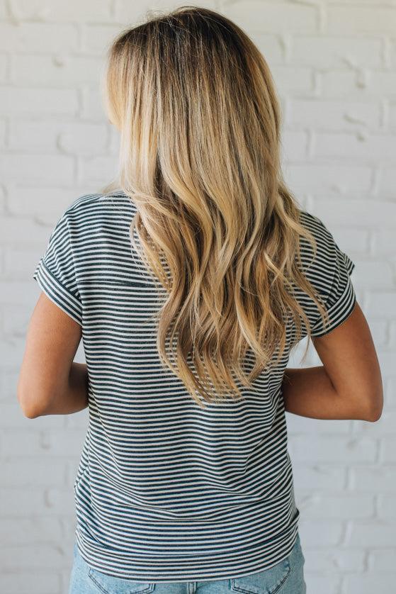 Blonde woman wearing a charcoal grey and white horizontal striped tee with a twist back keyhole accent across the back shoulders.