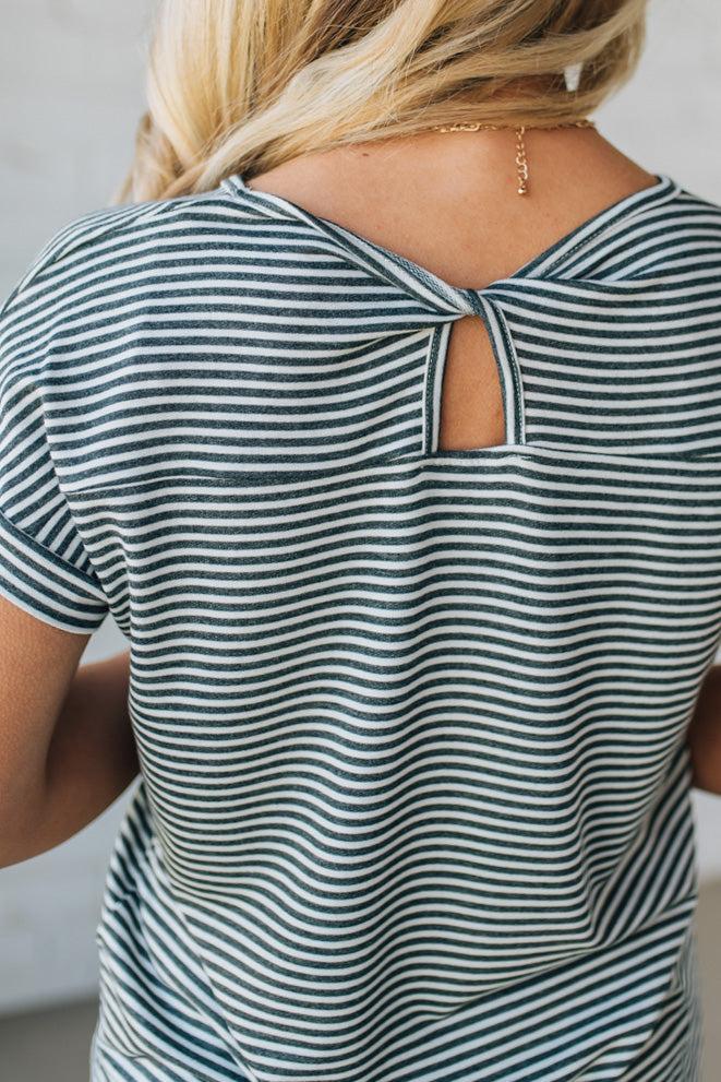 Blonde woman wearing a charcoal grey and white horizontal striped tee with a twist back keyhole accent across the back shoulders.