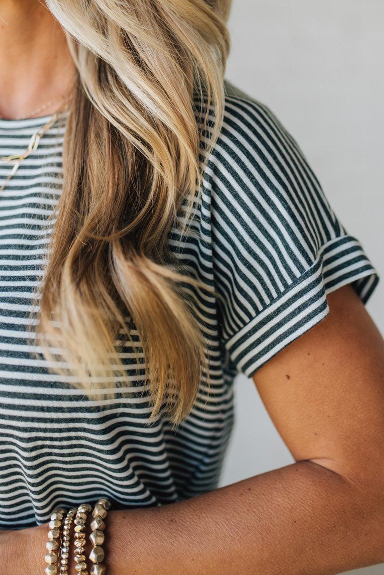 Blonde woman wearing a charcoal grey and white horizontal striped tee with a twist back keyhole accent across the back shoulders.
