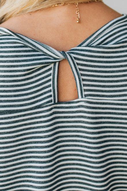 Blonde woman wearing a charcoal grey and white horizontal striped tee with a twist back keyhole accent across the back shoulders.
