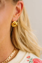 Gold knot earring worn by a person with a neutral background