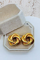 Pair of gold knot earrings on a beige jewelry display box.