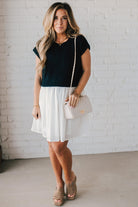 Blonde woman wearing a chic babydoll dress in black and white with a textured sweater upper, and flowy white lined skirt attached.