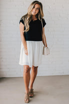 Blonde woman wearing a chic babydoll dress in black and white with a textured sweater upper, and flowy white lined skirt attached.