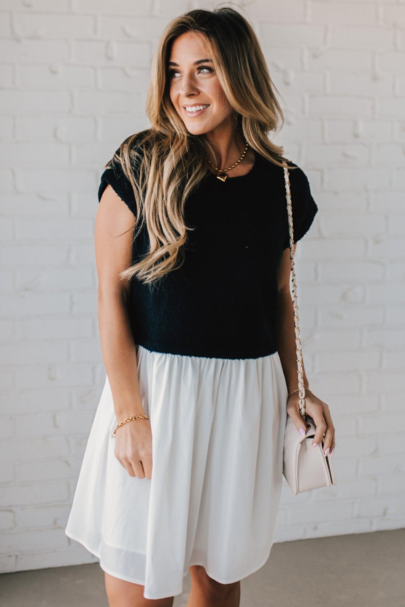 Blonde woman wearing a chic babydoll dress in black and white with a textured sweater upper, and flowy white lined skirt attached.