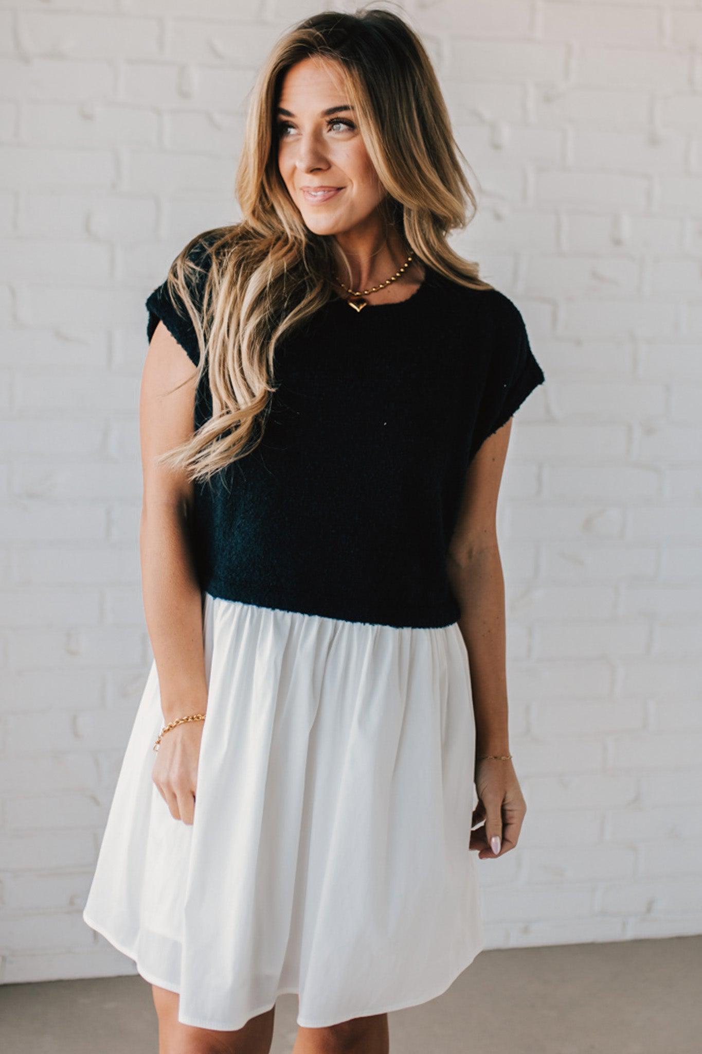 Blonde woman wearing a chic babydoll dress in black and white with a textured sweater upper, and flowy white lined skirt attached.