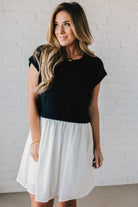 Blonde woman wearing a chic babydoll dress in black and white with a textured sweater upper, and flowy white lined skirt attached.