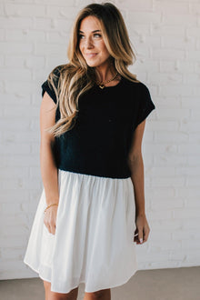  Blonde woman wearing a chic babydoll dress in black and white with a textured sweater upper, and flowy white lined skirt attached.