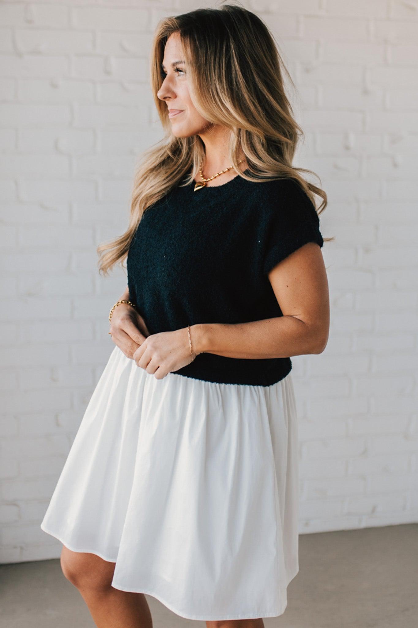 Blonde woman wearing a chic babydoll dress in black and white with a textured sweater upper, and flowy white lined skirt attached.