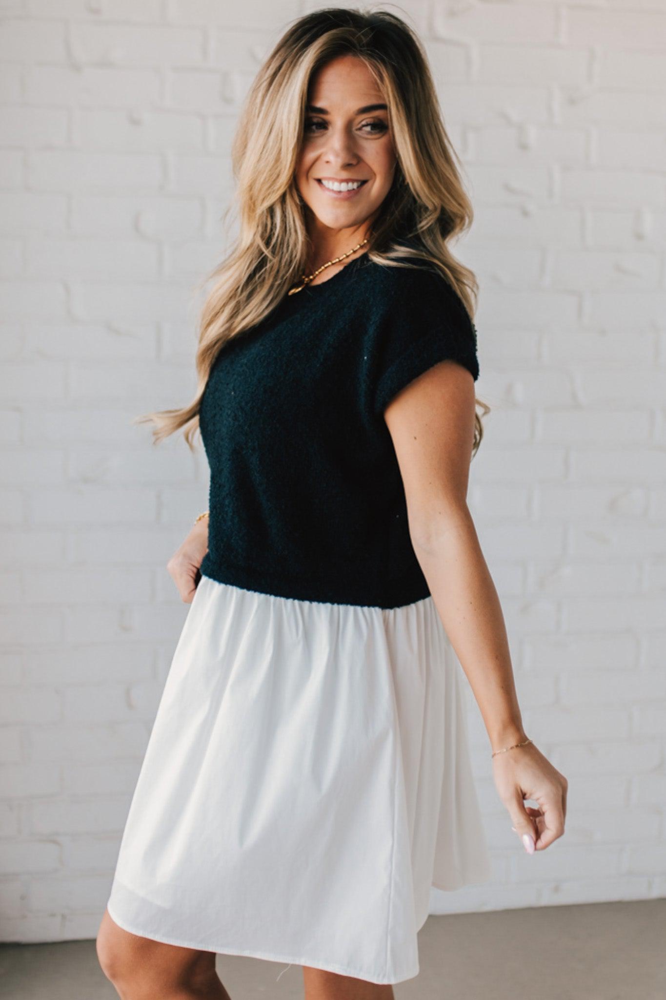 Blonde woman wearing a chic babydoll dress in black and white with a textured sweater upper, and flowy white lined skirt attached.