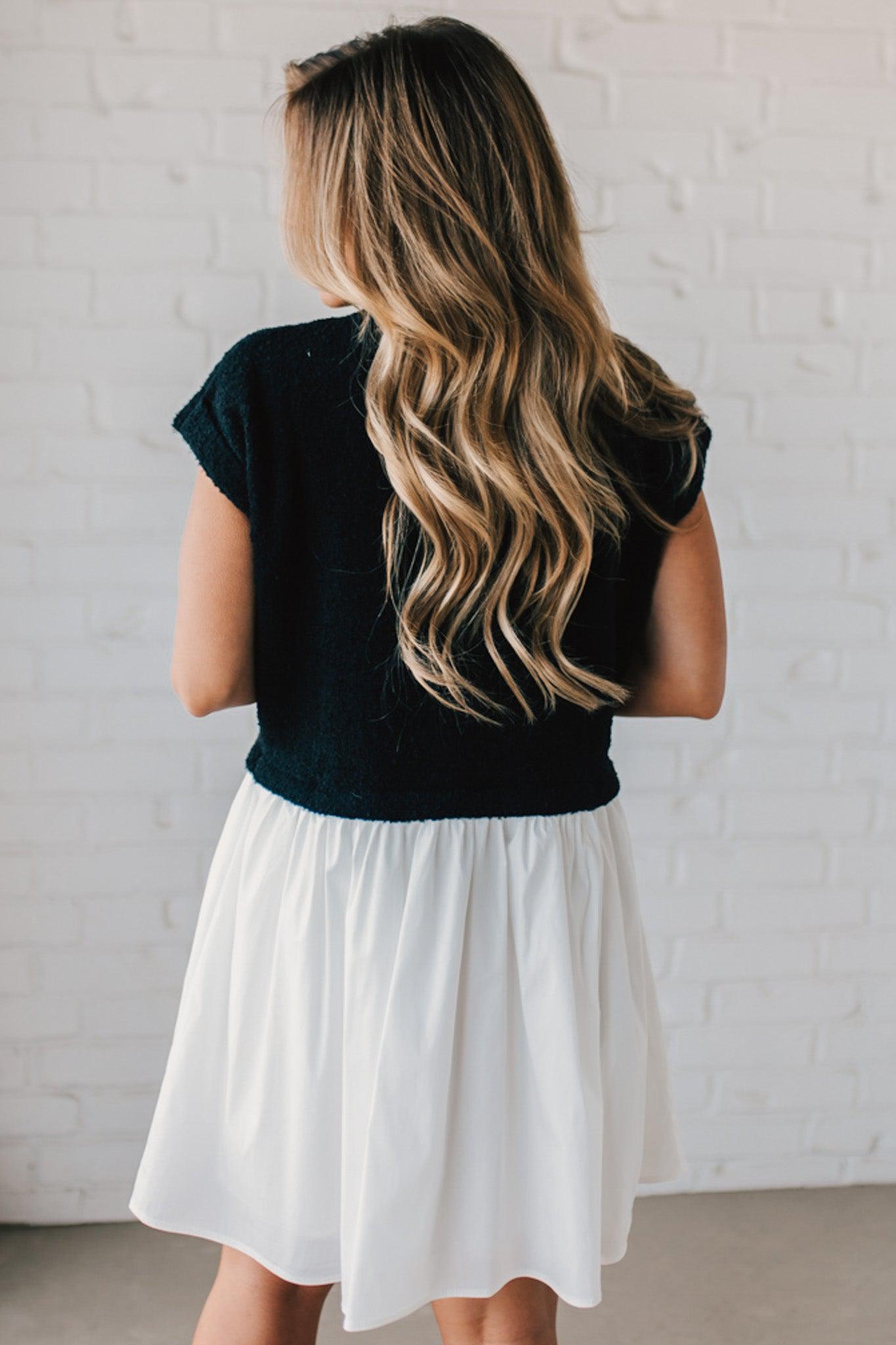 Blonde woman wearing a chic babydoll dress in black and white with a textured sweater upper, and flowy white lined skirt attached.